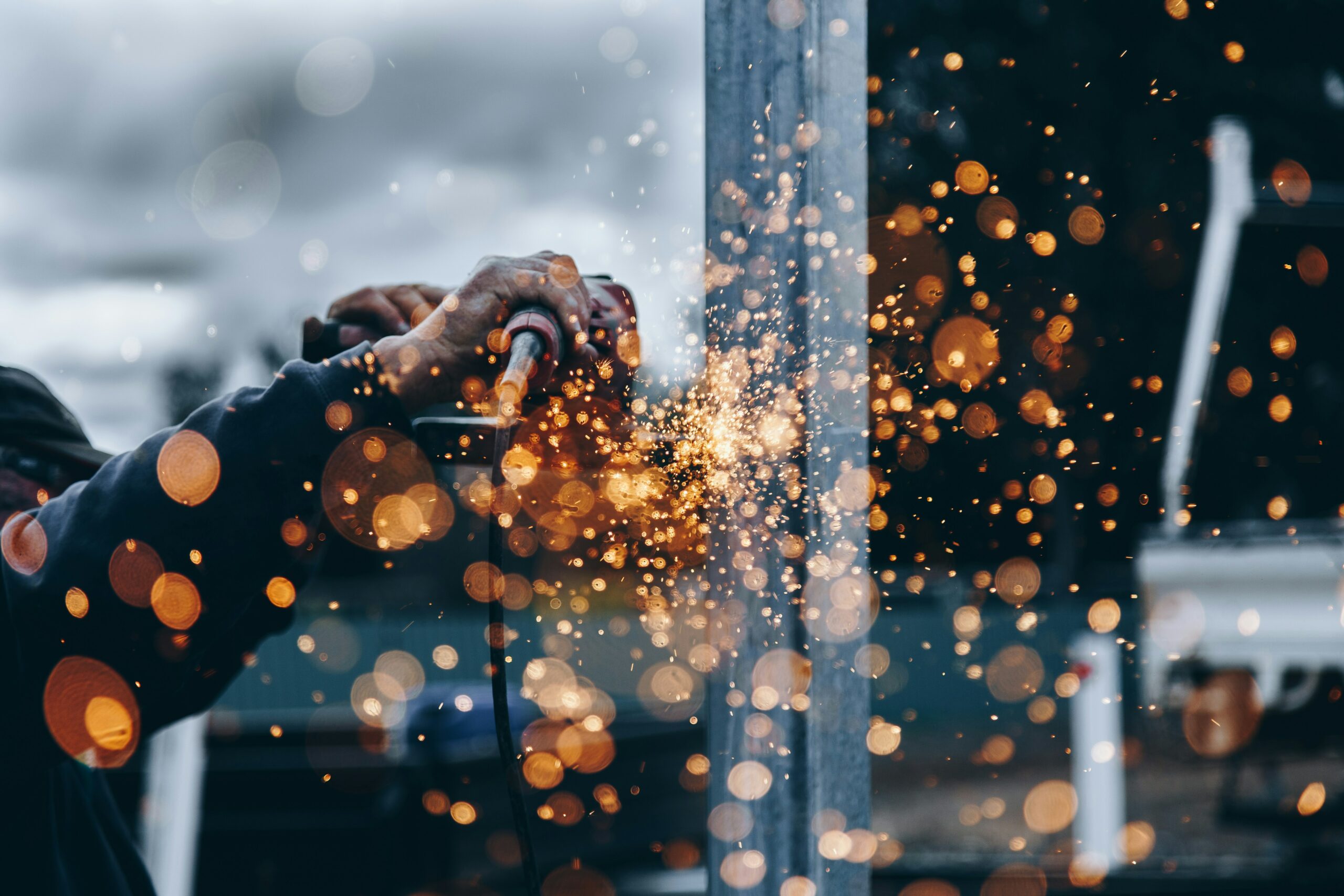 Ein Handwerker bearbeitet ein Werkstück, es sprüht gelbe und goldene Funken, die durch Objektivunschärfe ästhetische Flecken auf dem Foto ergben